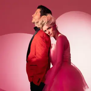 Two models posing in front of a pink heart background