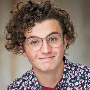 Curly hair man with glasses giving a cheeky half smile in a floral print shirt