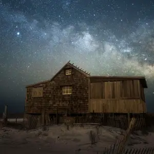 Shack on a beach at night with the milky way in the sky behind it