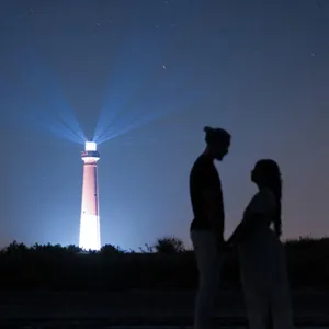 A couple silhouetted against a night sky with a lighthouse in the background