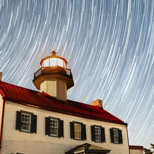 A lighthouse with stars swirling behind it in the night sky