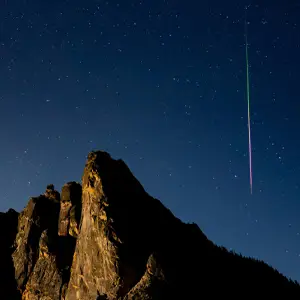 Mountains with starry night sky and a streak of colorful light