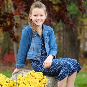 a kid in a blue denim jacket poses on a rock