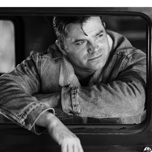 man in a jacket sits relaxing out of the window of a car door