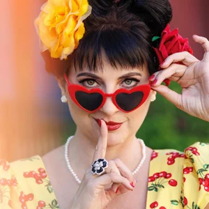 vibrant portrait of a woman wearing red heart sunglasses touching her lips with a finger