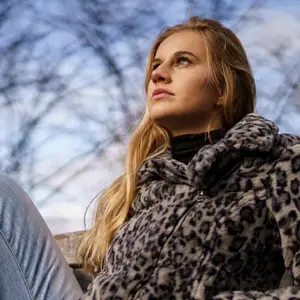 Woman in a white leopard print jacket, staring up at the sky