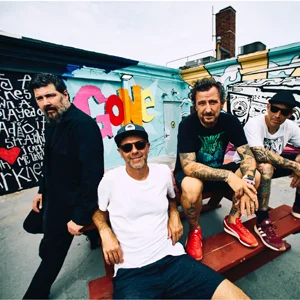 A band poses on a picnic bench in a graffiti'd skatepark