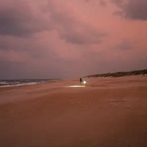 Two people with a flashlight on the beach at dusk