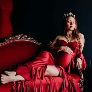 Pregnant model sits on lounge draped in red silk