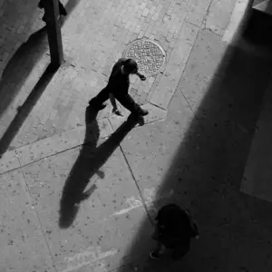 Overhead view of a man and his shadow walking on the street below 