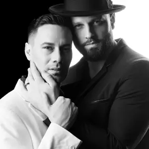 Black and white portrait of two men holding one another, one dressed in white and the other in black