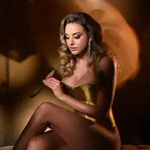 Model in a corset, sitting with crossed legs and looking down while holding a parasol