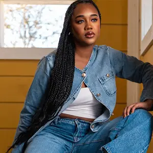 Woman with long braids and a denim outfit, staring off-camera