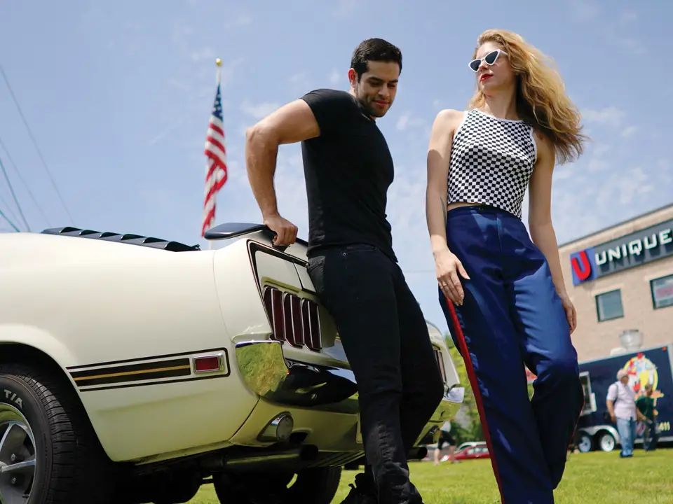 two models pose on the trunk of a classic car