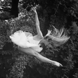 Ballerina in white tutu jumping outside with toes pointed